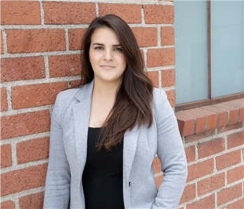 a woman in a grey blazer in front of a brick wall